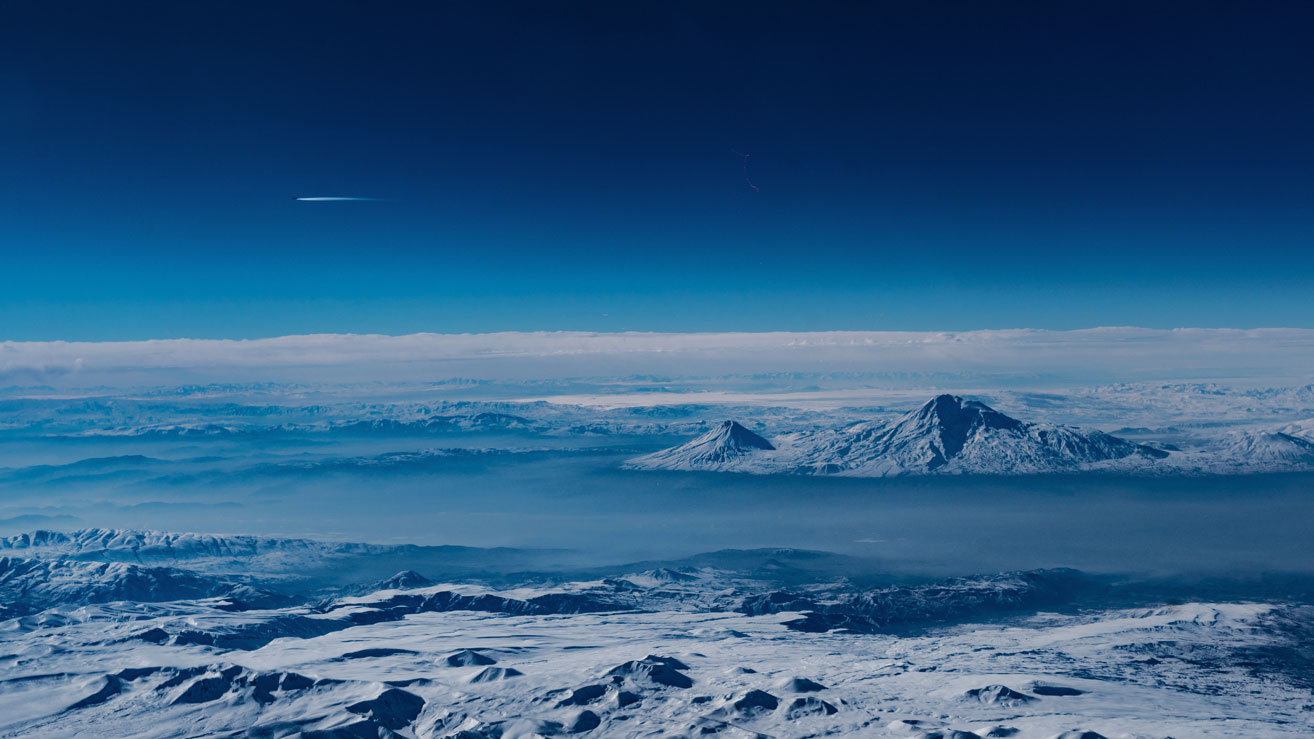 AGU space over mountains header Looking out over cold snowy mountains from a plane